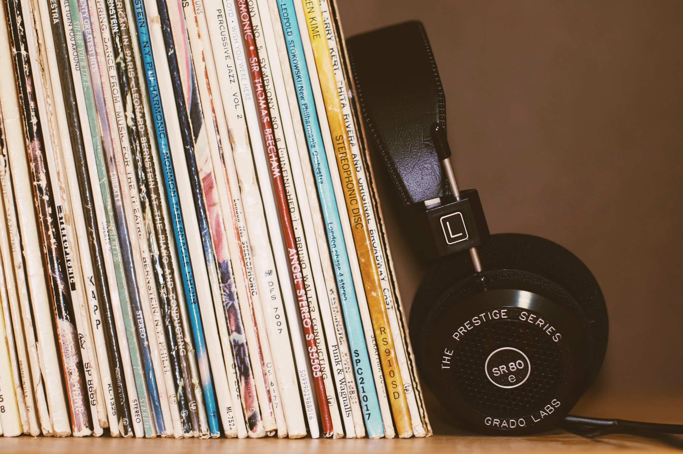 A stack of vintage records on a shelf beside a pair of headphones